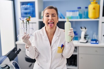 Wall Mural - Middle age hispanic woman working at cosmetics laboratory sticking tongue out happy with funny expression.