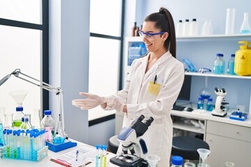 Wall Mural - Young beautiful hispanic woman scientist smiling confident wearing gloves at laboratory