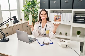 Sticker - Hispanic doctor woman holding model of human anatomical skin and hair sticking tongue out happy with funny expression.