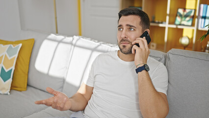 Canvas Print - Young hispanic man talking on smartphone sitting on sofa at home