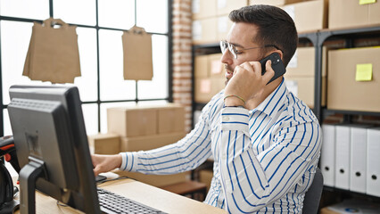 Wall Mural - Young hispanic man ecommerce business worker talking on smartphone using computer at office