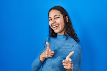 Poster - Young brazilian woman standing over blue isolated background pointing fingers to camera with happy and funny face. good energy and vibes.