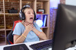 Young caucasian woman playing video games wearing headphones shouting suffocate because painful strangle. health problem. asphyxiate and suicide concept.