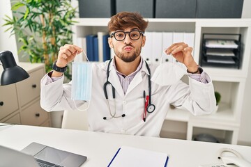 Canvas Print - Arab man with beard wearing doctor uniform holding medical mask looking at the camera blowing a kiss being lovely and sexy. love expression.