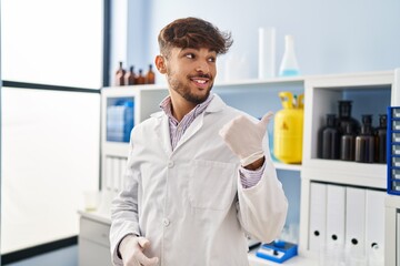 Sticker - Arab man with beard working at scientist laboratory pointing thumb up to the side smiling happy with open mouth