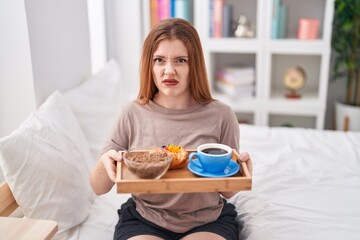 Canvas Print - Redhead woman wearing pajama holding breakfast tray clueless and confused expression. doubt concept.