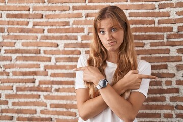 Sticker - Young caucasian woman standing over bricks wall pointing to both sides with fingers, different direction disagree