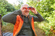 Senior man bird watching with binoculars in autumn forest