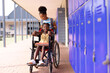 Happy african american schoolgirl in wheelchair with her friend in school yard