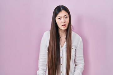 Wall Mural - Chinese young woman standing over pink background in shock face, looking skeptical and sarcastic, surprised with open mouth