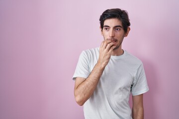 Canvas Print - Young hispanic man standing over pink background looking stressed and nervous with hands on mouth biting nails. anxiety problem.