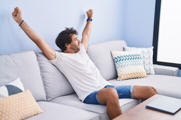 Poster - Young hispanic man stretching arms sitting on sofa at home