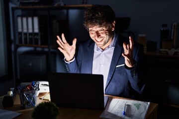 Canvas Print - Hispanic young man working at the office at night celebrating crazy and amazed for success with arms raised and open eyes screaming excited. winner concept