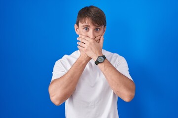 Sticker - Caucasian blond man standing over blue background shocked covering mouth with hands for mistake. secret concept.