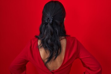 Poster - Asian young woman standing over red background standing backwards looking away with arms on body