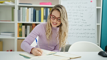 Wall Mural - Young blonde woman student smiling confident writing on notebook at classroom