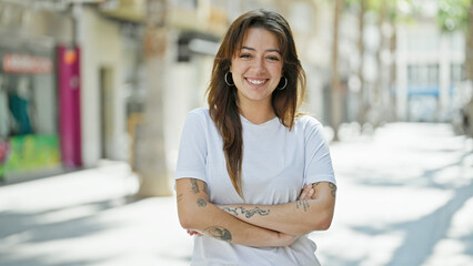 Wall Mural - Young beautiful hispanic woman smiling confident standing with arms crossed gesture at street