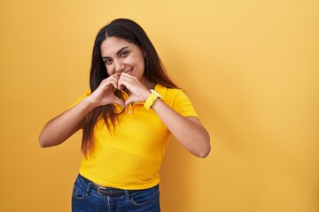 Wall Mural - Young arab woman standing over yellow background smiling in love doing heart symbol shape with hands. romantic concept.