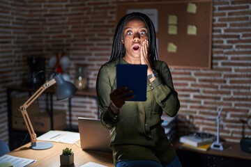 Wall Mural - Young african american with braids working at the office at night afraid and shocked, surprise and amazed expression with hands on face