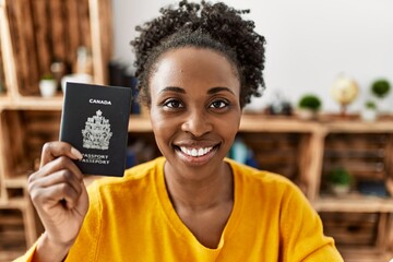 Canvas Print - African american woman holding canada passport sitting on table at home