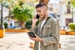 © Krakenimages.com - Young hispanic man talking on the smartphone reading passport at park