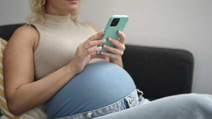 Poster - Young pregnant woman using smartphone sitting on sofa at home