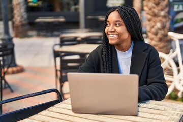 Wall Mural - African american woman using laptop sitting on table at coffee shop terrace