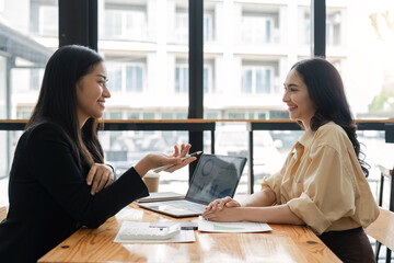 Wall Mural - Happy two beautiful young Asian businesswoman standing discuss working together at office