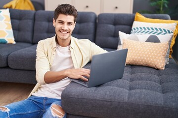 Wall Mural - Young hispanic man using laptop sitting on floor at home