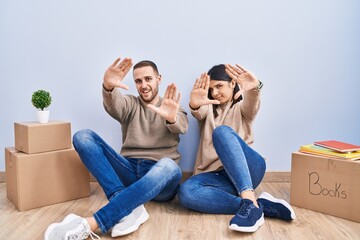 Poster - Young couple moving to a new home doing frame using hands palms and fingers, camera perspective