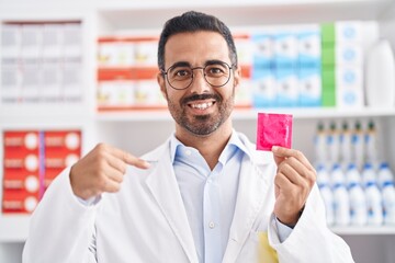 Wall Mural - Hispanic man with beard working at pharmacy drugstore holding condom pointing finger to one self smiling happy and proud