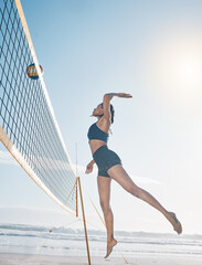 Woman, jump and volleyball player on beach by net in serious sports match, game or competition. Fit, active and sporty female person jumping or reaching for ball in volley or spike by the ocean coast