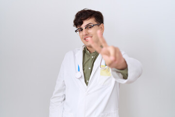 Poster - Young non binary man wearing doctor uniform and stethoscope smiling looking to the camera showing fingers doing victory sign. number two.