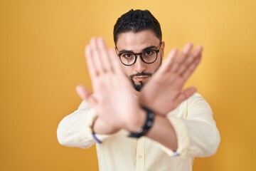 Poster - Hispanic young man wearing business clothes and glasses rejection expression crossing arms and palms doing negative sign, angry face