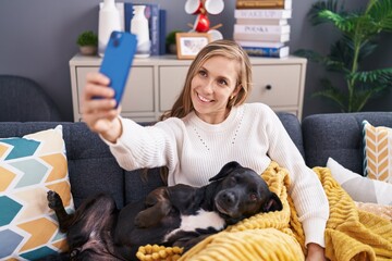 Poster - Young blonde woman make selfie by smartphone sitting on sofa with dog at home