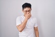 © Krakenimages.com - Young asian man standing over white background smelling something stinky and disgusting, intolerable smell, holding breath with fingers on nose. bad smell