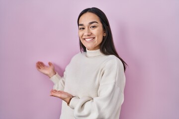 Poster - Young south asian woman standing over pink background inviting to enter smiling natural with open hand