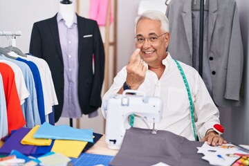 Wall Mural - Middle age man with grey hair dressmaker using sewing machine beckoning come here gesture with hand inviting welcoming happy and smiling