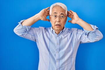 Wall Mural - Hispanic senior man wearing glasses crazy and scared with hands on head, afraid and surprised of shock with open mouth