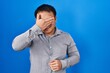© Krakenimages.com - Young chinese man standing over blue background smiling and laughing with hand on face covering eyes for surprise. blind concept.
