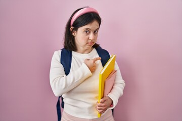 Poster - Woman with down syndrome wearing student backpack and holding books pointing with hand finger to the side showing advertisement, serious and calm face