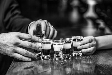 Group friends tequila shot glasses in bar. Male hands glasses of shot or liqueur. Friends drink shot or liqueur. Black and white