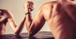 © Yevhen - Two man's hands clasped arm wrestling, strong and weak, unequal match. Arm wrestling. Heavily muscled bearded man arm wrestling a puny weak man