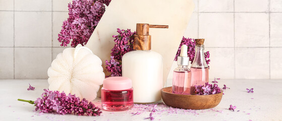 Bottle of liquid soap with serum, cosmetic gel, bast wisp and lilac flowers on light background