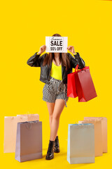 Young woman holding paper with text SUMMER SALE and shopping bags on yellow background