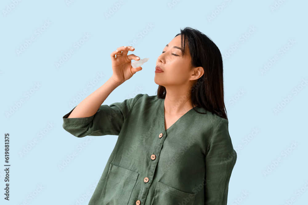Allergic Asian woman with nasal drops on blue background