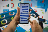 Fototapeta  - Ręka trzymająca telefon z białym ekranem i z powiększonym przez lupę napisem social media na tle wykresów.