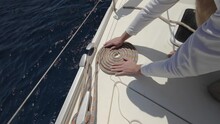 Close-up Footage Of Sailboat Ropes, Pulleys And Ropes On The Mast. A Yachtsman Coils, Winds A Rope On Deck. Floating Sailing Yacht With Spread Sails. Boat Cutting Through The Sea. Summer Vacation