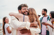 © Jose Calsina - Happy man and excited woman hugging at a party with a group of people at friendly meeting. Thankful guy embracing his female best friend. Male giving a grateful affectionate greeting. Couple bonding