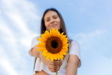 mujer joven, sonriendo y sosteniendo un girasol en un día soleado de primavera en un parque, enfoque selectivo, concepto de alegría, y belleza en primavera. paz, girasoles gigantes y amarillos.